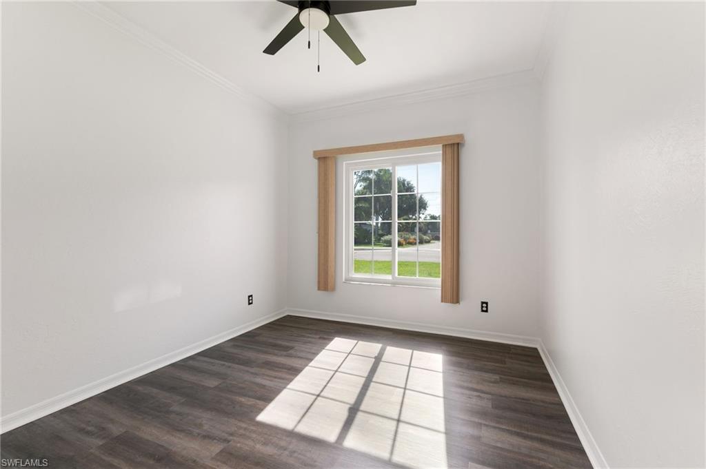 Bright room featuring a large window with exterior views, dark wood-finish flooring, white walls, and a ceiling fan
