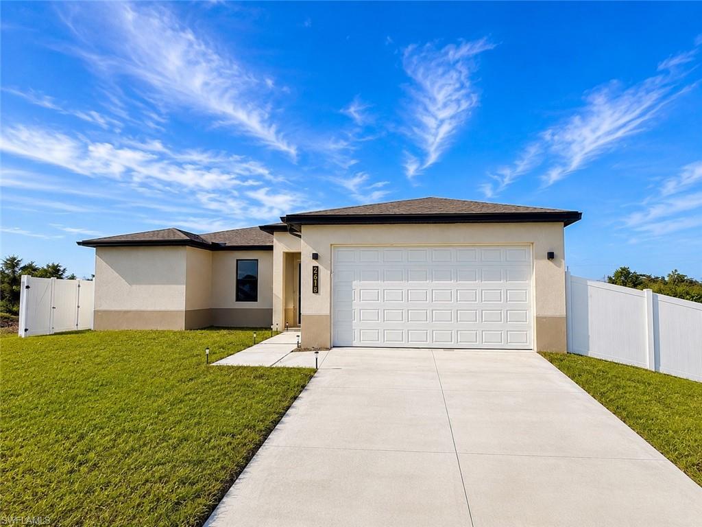 Contemporary stucco exterior featuring a dark asphalt shingle roof, integrated single-car garage, and a lush, landscaped front yard with mature palms and varied plantings