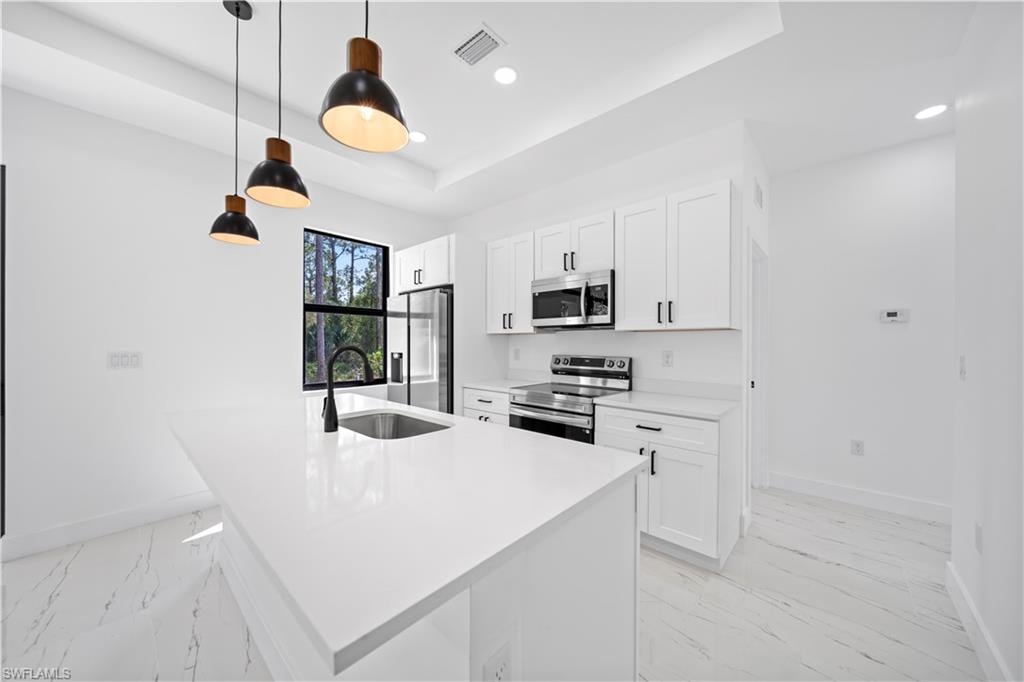 Open-concept living space featuring a kitchen with white cabinetry and stainless steel appliances, a center island with pendant lighting, and recessed ceiling lights