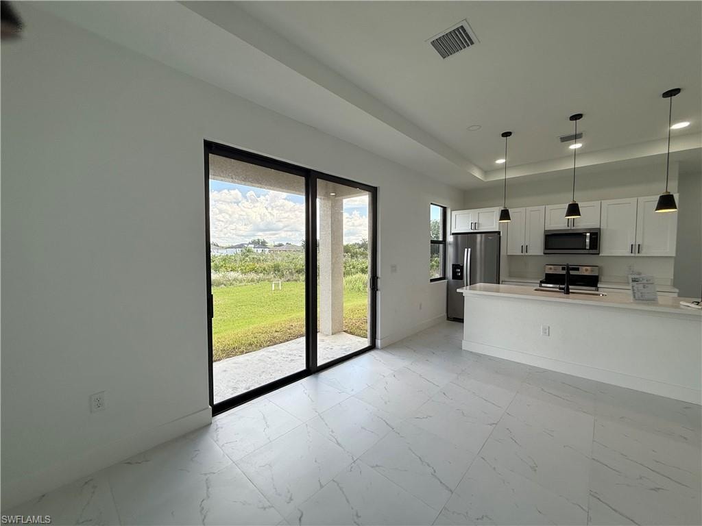 Modern kitchen featuring a central island with an integrated sink, white cabinetry, integrated stainless steel appliances, pendant lighting, and wood-finish flooring