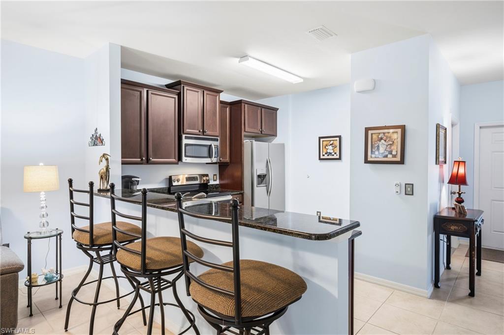 Kitchen area featuring a granite-style countertop breakfast bar, dark wood-finish cabinetry, a stainless steel microwave, and a stainless steel refrigerator