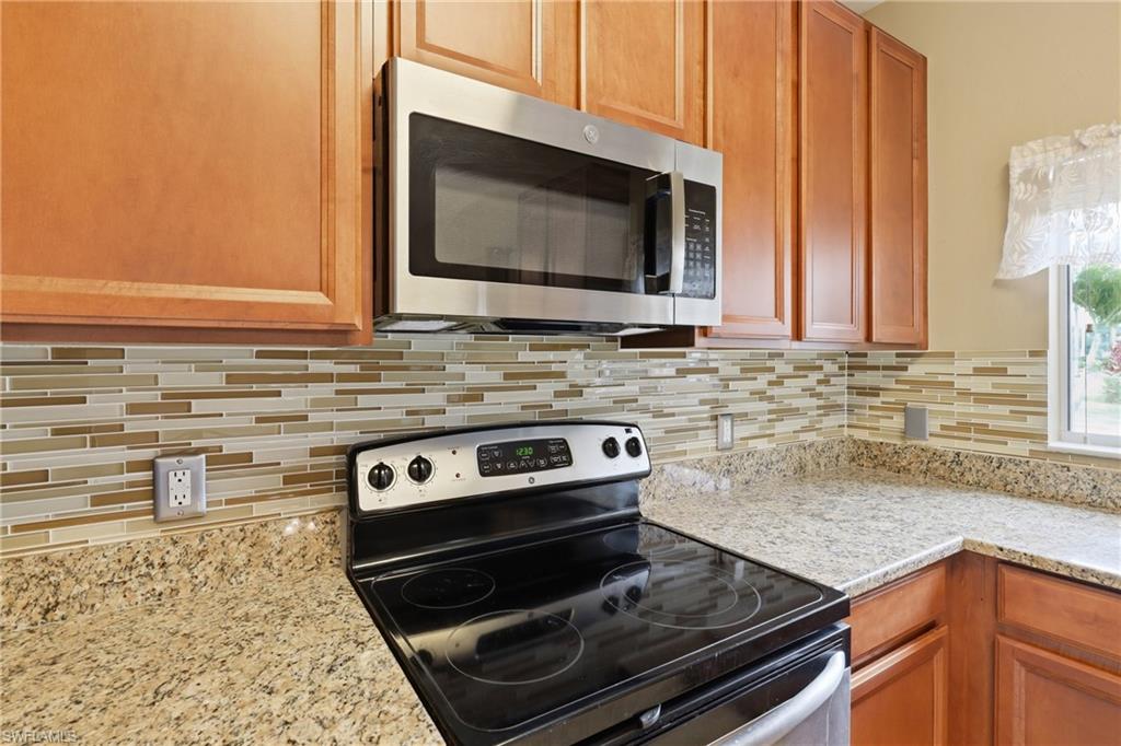 Kitchen area featuring wood cabinetry, stainless steel microwave, black electric range, granite countertops, and a mosaic tile backsplash