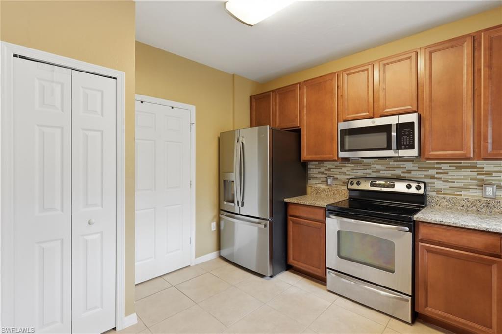 Functional kitchen featuring stainless steel appliances, light wood-finish cabinetry, granite-style countertops, and a mosaic tile backsplash