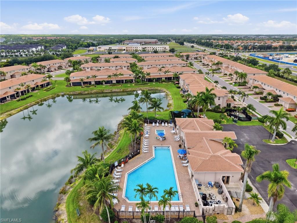 Community swimming pool with surrounding lounge seating, a nearby building with a covered patio, and a perimeter fence