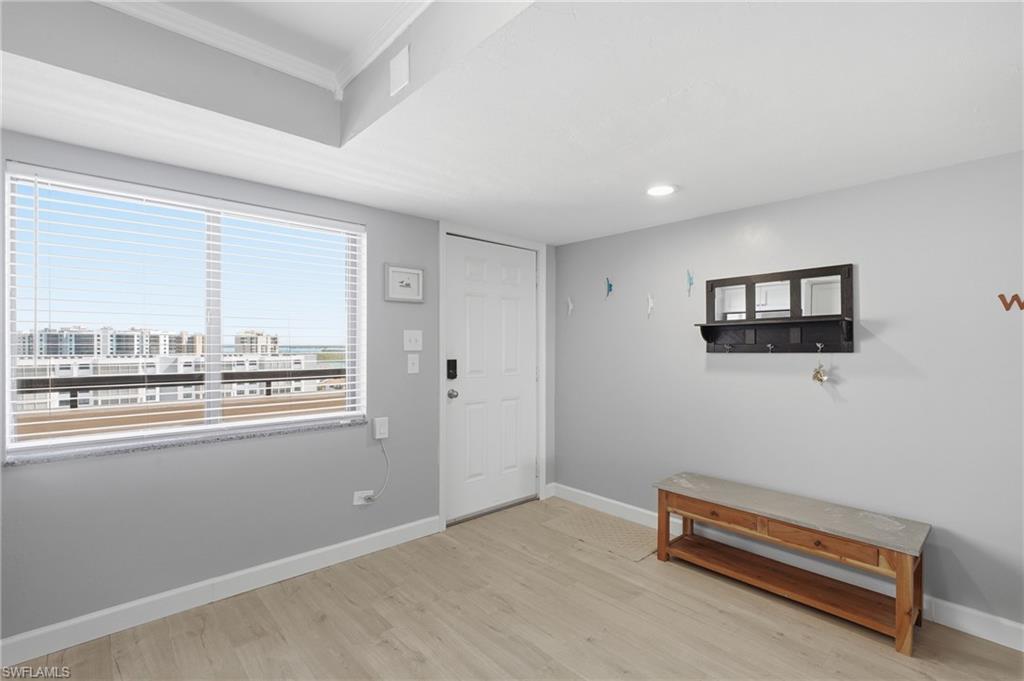 Bright entry area featuring a large window with horizontal blinds, light wood-finish flooring, a white paneled door, recessed lighting, and white baseboards - Virtually Edited Image