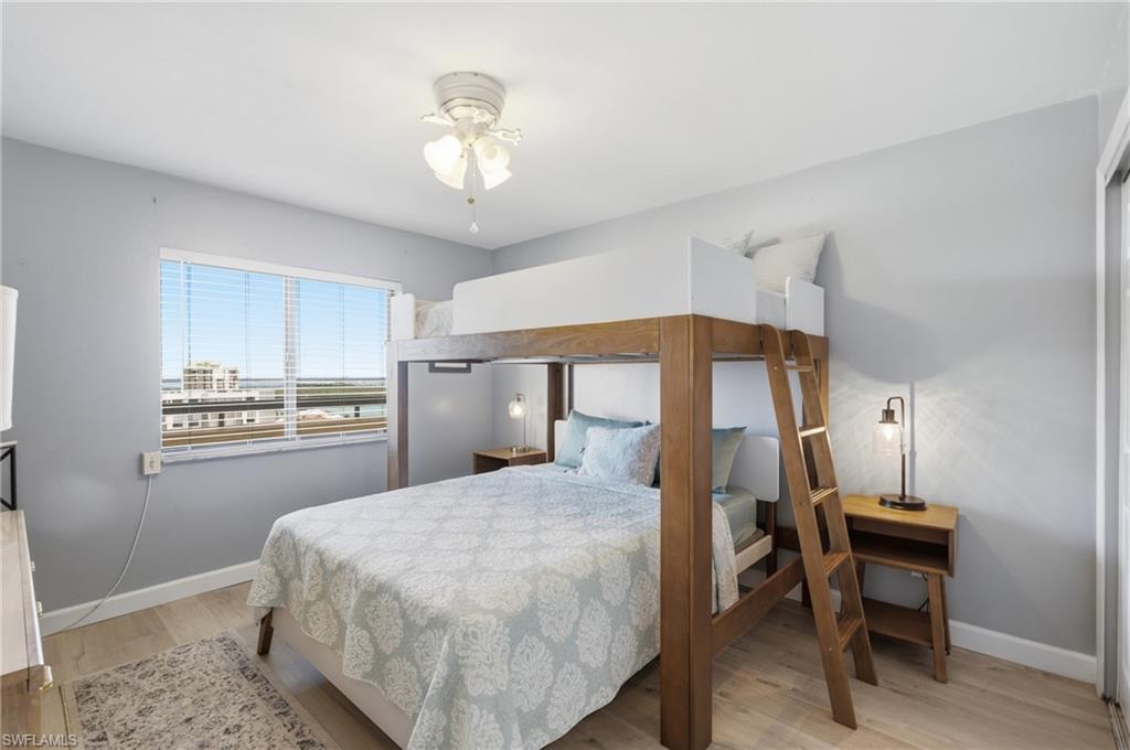 Light-filled bedroom featuring a wood-finish bunk bed, pale wood-finish flooring, and a ceiling fan with light fixture - Virtually Edited Image