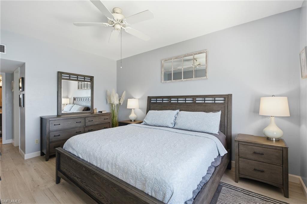 Bedroom featuring light wood-finish flooring, a white ceiling fan with integrated lighting, and light gray wall paint - Virtually Edited Image