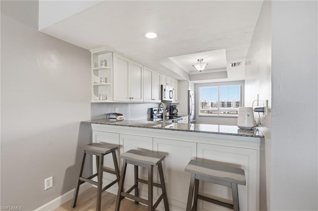 Well-appointed kitchen featuring white cabinetry, granite countertops, stainless steel appliances, and a breakfast bar - Virtually Edited Image