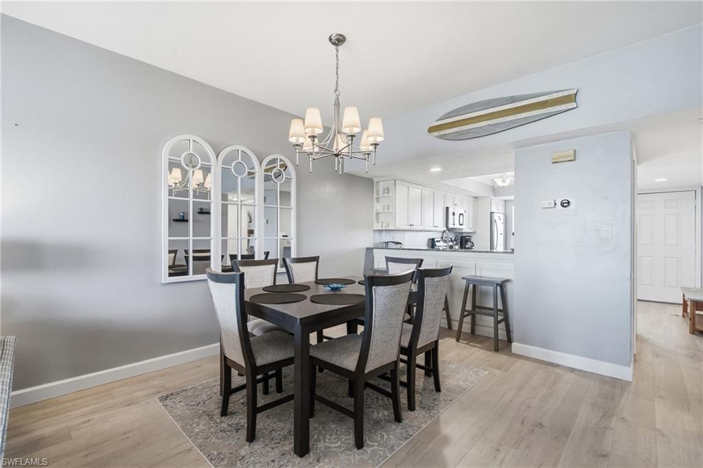 Dining area with wood-finish flooring, a contemporary chandelier, and a decorative mirror triptych - Virtually Edited Image