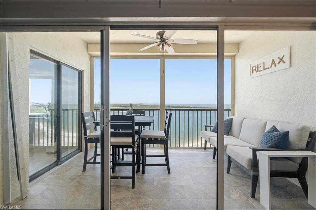 Expansive screened balcony featuring a ceiling fan, tiled flooring, and panoramic water and coastline views - Virtually Edited Image