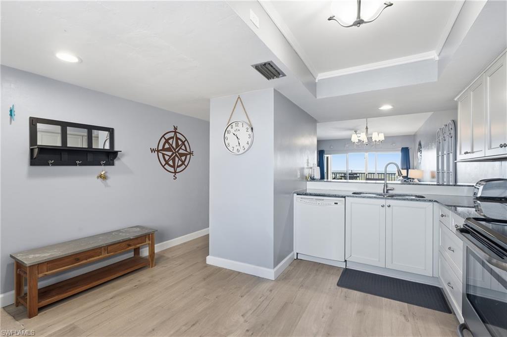 Kitchen featuring white cabinetry, granite countertops, stainless steel sink, and wood-finish flooring - Virtually Edited Image