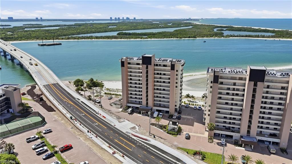 Waterfront high-rise building featuring multiple balconies, direct access to a sandy shoreline, and proximity to a bridge - Virtually Edited Image
