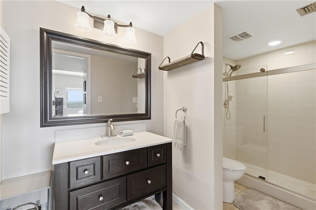 Bathroom featuring a dark wood vanity with a white countertop, framed mirror, three-light fixture, and a glass-enclosed shower with tiled walls - Virtually Edited Image