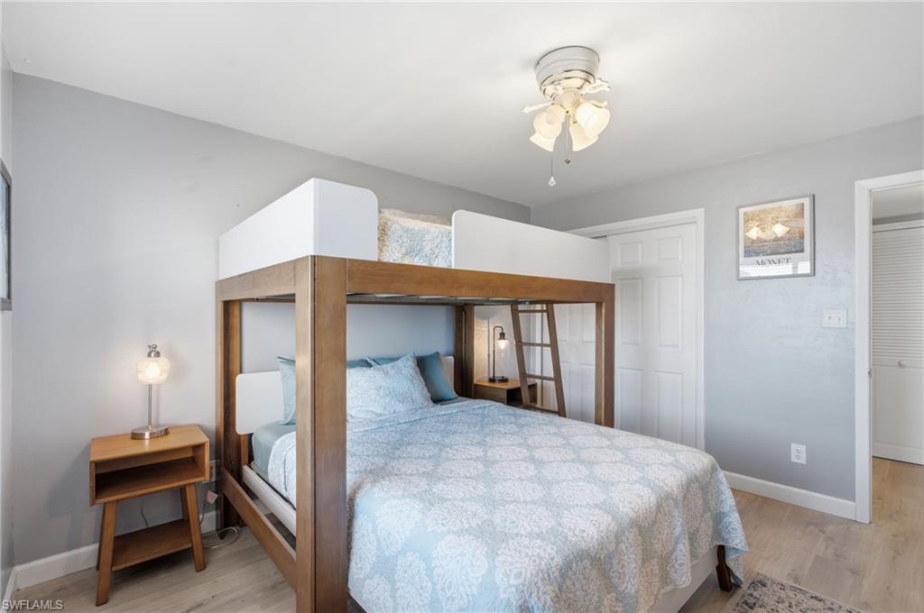 Room featuring a built-in bunk bed with a wooden frame and white accents, light gray walls, and wood-finish flooring - Virtually Edited Image