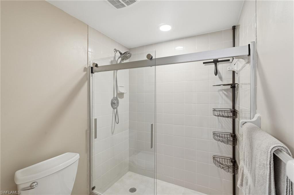 Glass-enclosed shower featuring white subway tile surround, a rain shower head, and a handheld sprayer - Virtually Edited Image