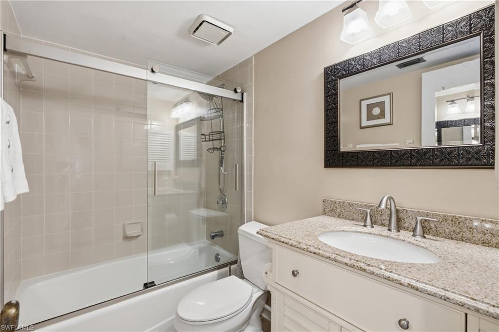 Bathroom featuring a combination tub and shower with glass sliding doors, neutral-toned wall tiles, and a white vanity with a light-colored countertop - Virtually Edited Image