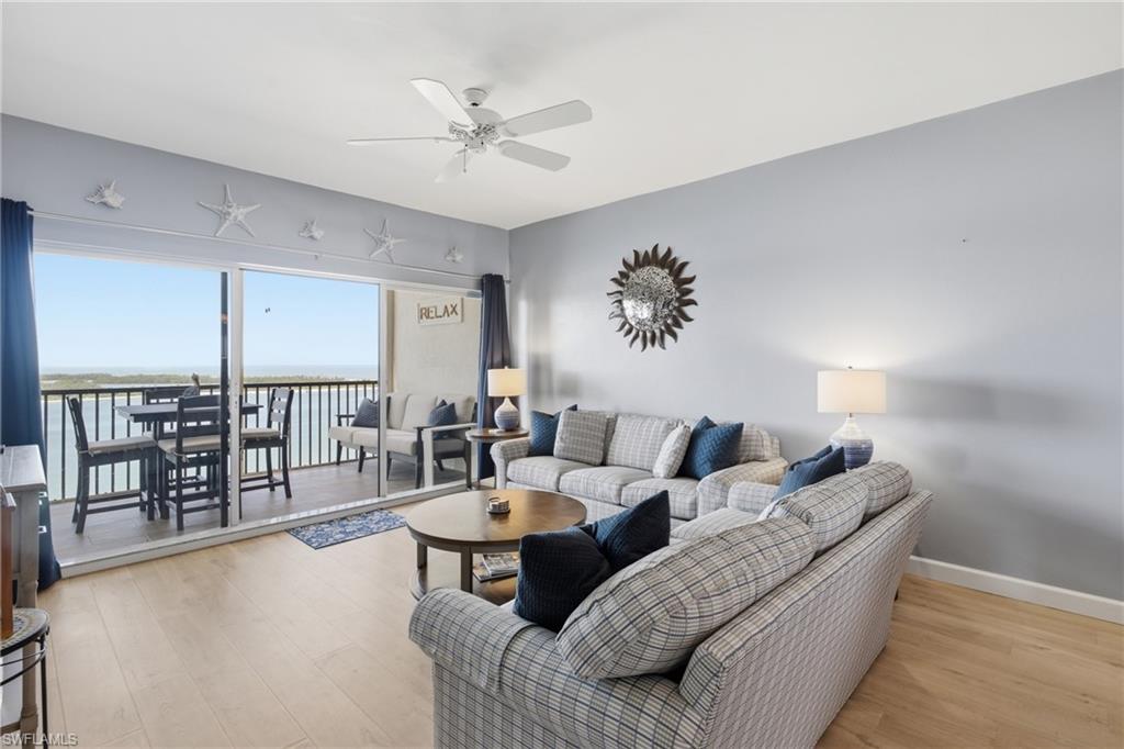 Spacious living area featuring light wood-finish flooring, a ceiling fan, and direct access to a private balcony through a large sliding glass door - Virtually Edited Image