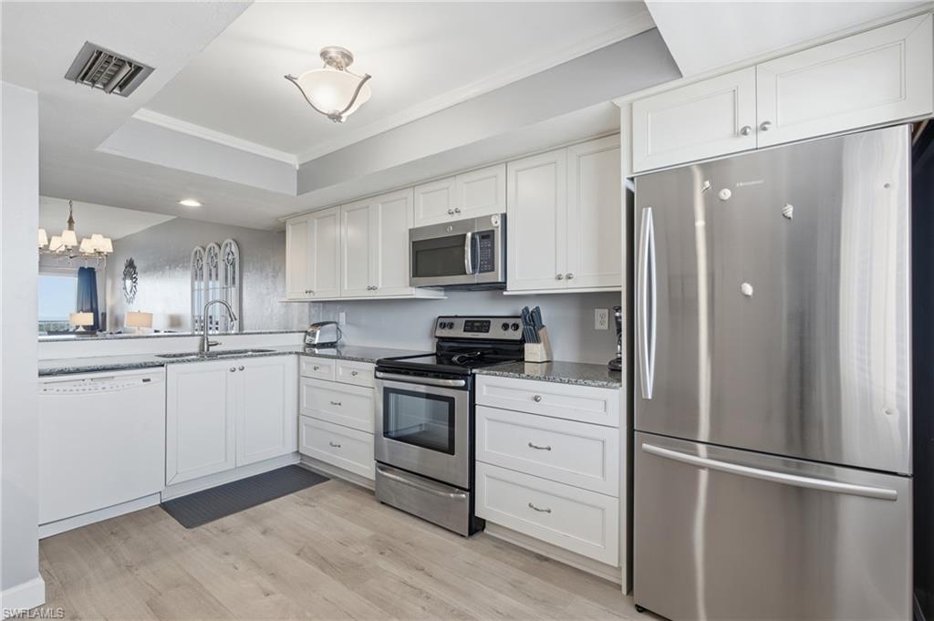 Kitchen featuring white cabinetry, stainless steel appliances, dark stone countertops, wood-finish flooring, and a contemporary ceiling light fixture - Virtually Edited Image