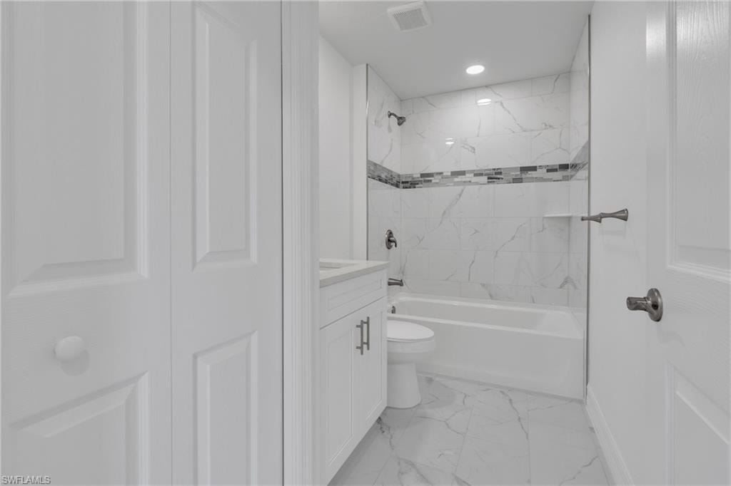 Bathroom featuring a white vanity with integrated sink, white marble-look tile flooring, and white marble-look shower surround with an accent mosaic tile band and built-in shelf