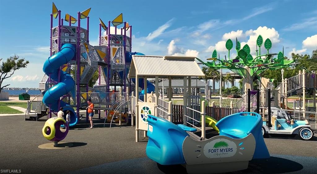 Spacious playground featuring a multi-level climbing structure with blue spiral slides, a smaller play area with a covered structure, an ornamental tree sculpture, and a novelty car play feature