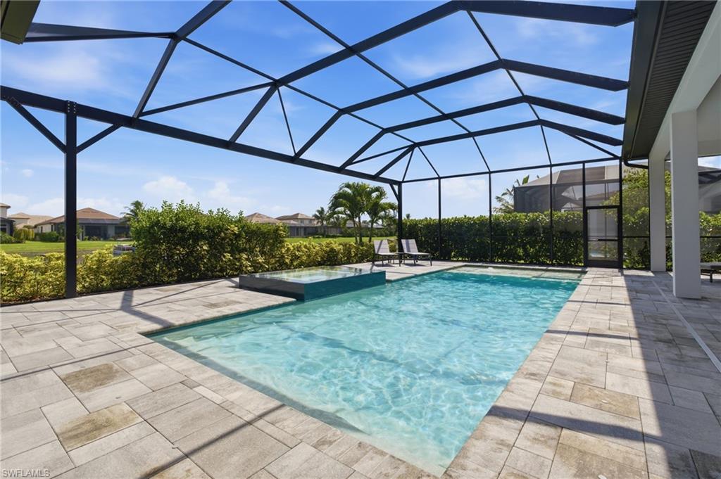 Screen-enclosed outdoor living area featuring a rectangular swimming pool with an integrated spa, complemented by a paver patio