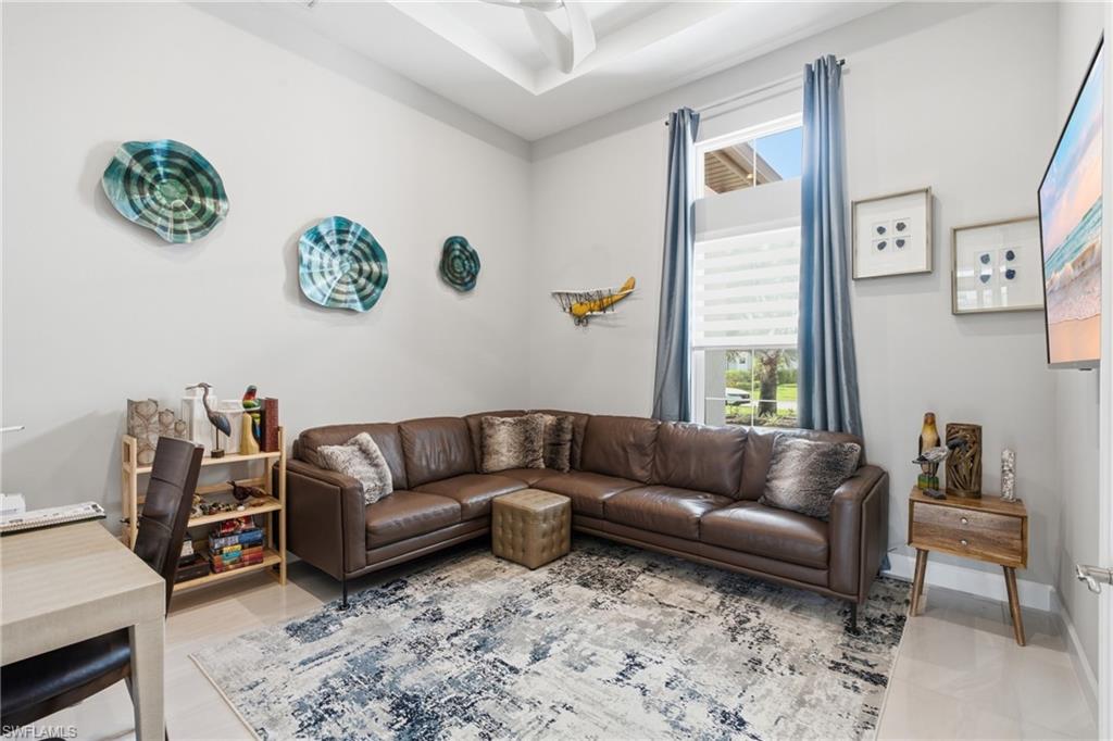 Living area featuring a tray ceiling with a ceiling fan, a large window with blinds and drapes, light-colored walls, and tile flooring