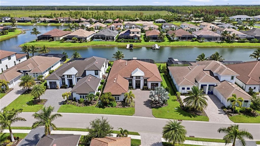 Waterfront property featuring a paver driveway, lush green lawns, mature palm trees, and a private dock