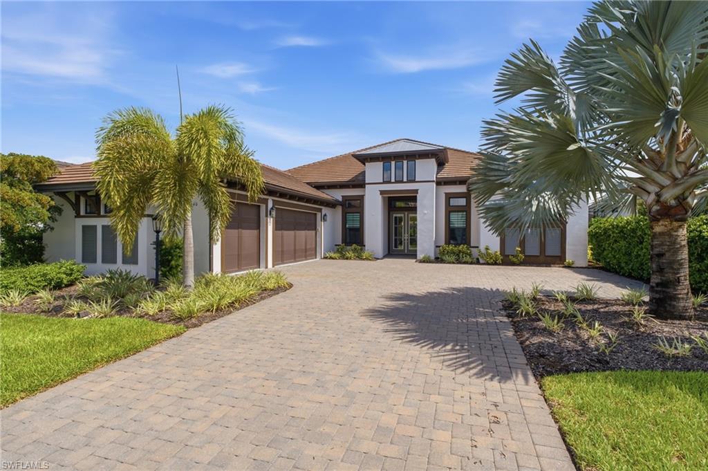 Exterior featuring a paver driveway, white stucco finish, brown roof tiles, multiple garage doors, and mature landscaping