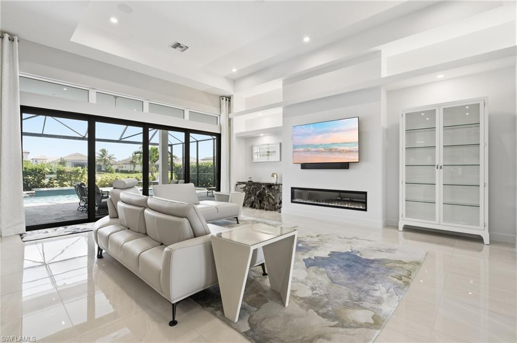Spacious living area featuring large format polished tile flooring, a built-in linear electric fireplace, and expansive sliding glass doors opening to a screened lanai with a pool