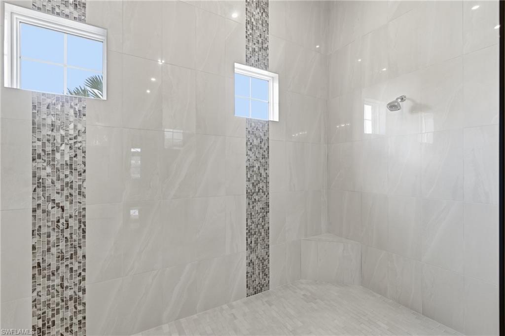 Spacious shower enclosure featuring large-format tile walls, decorative vertical mosaic tile accents, and integrated windows