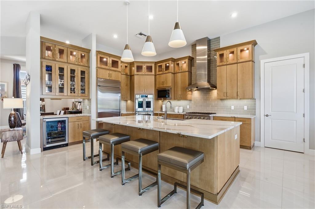 Gourmet kitchen featuring a large central island with seating, stainless steel appliances, extensive wood cabinetry, a tile backsplash, and polished tile flooring
