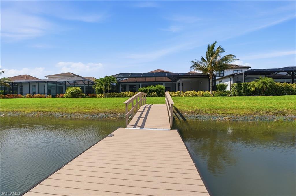 Waterfront property featuring a private boat dock, expansive green lawn, and mature tropical landscaping