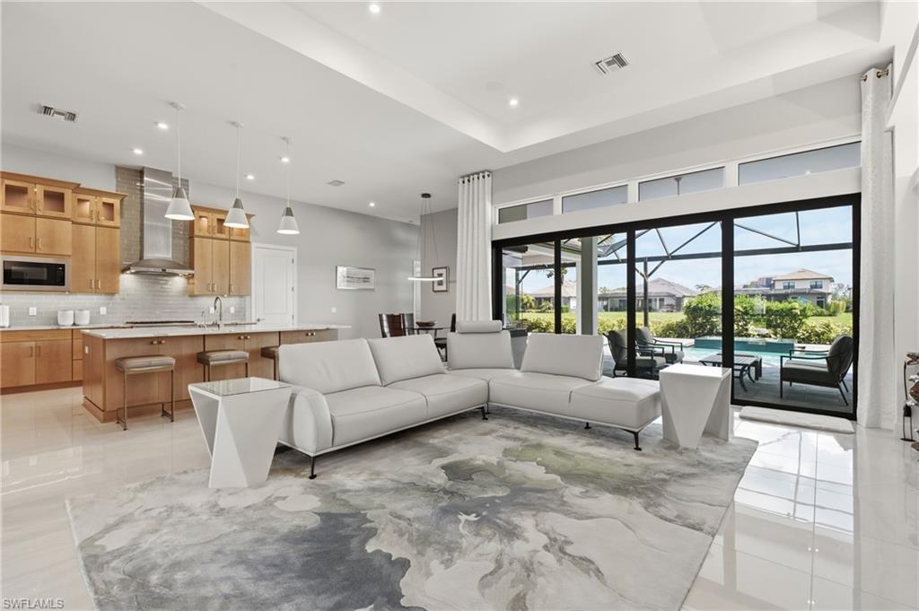 Open-concept living area featuring high ceilings, light wood cabinetry, a center island with seating, and a screened lanai with a swimming pool