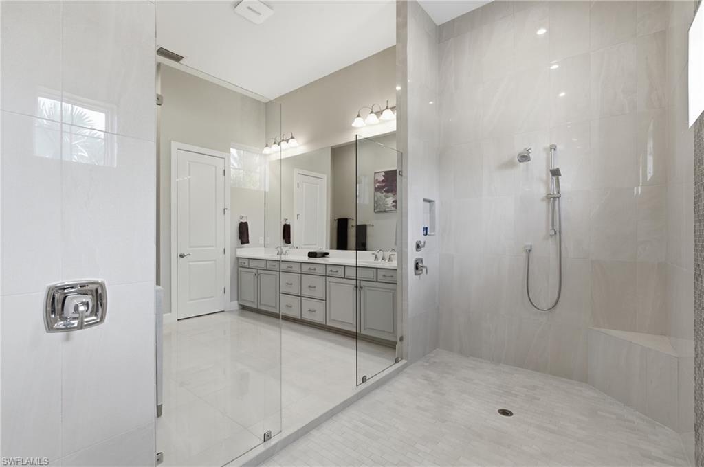 Spacious bathroom featuring a frameless glass shower enclosure with a built-in bench and a dual vanity with light gray cabinetry and a white countertop