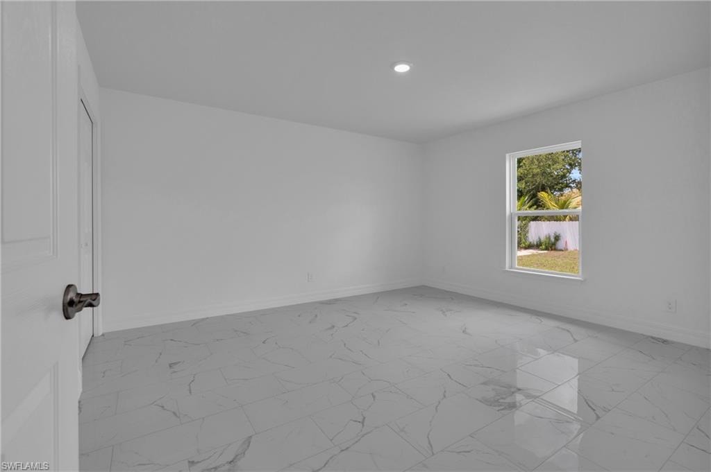 Spacious room featuring large format tile flooring, a window offering exterior views, a recessed ceiling light, and a white interior door with dark hardware