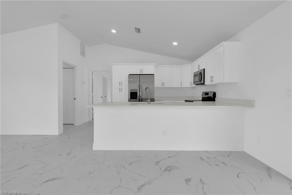 Modern kitchen featuring white shaker cabinetry, stainless steel appliances, a light-toned countertop, a kitchen island with a breakfast bar, and vaulted ceilings