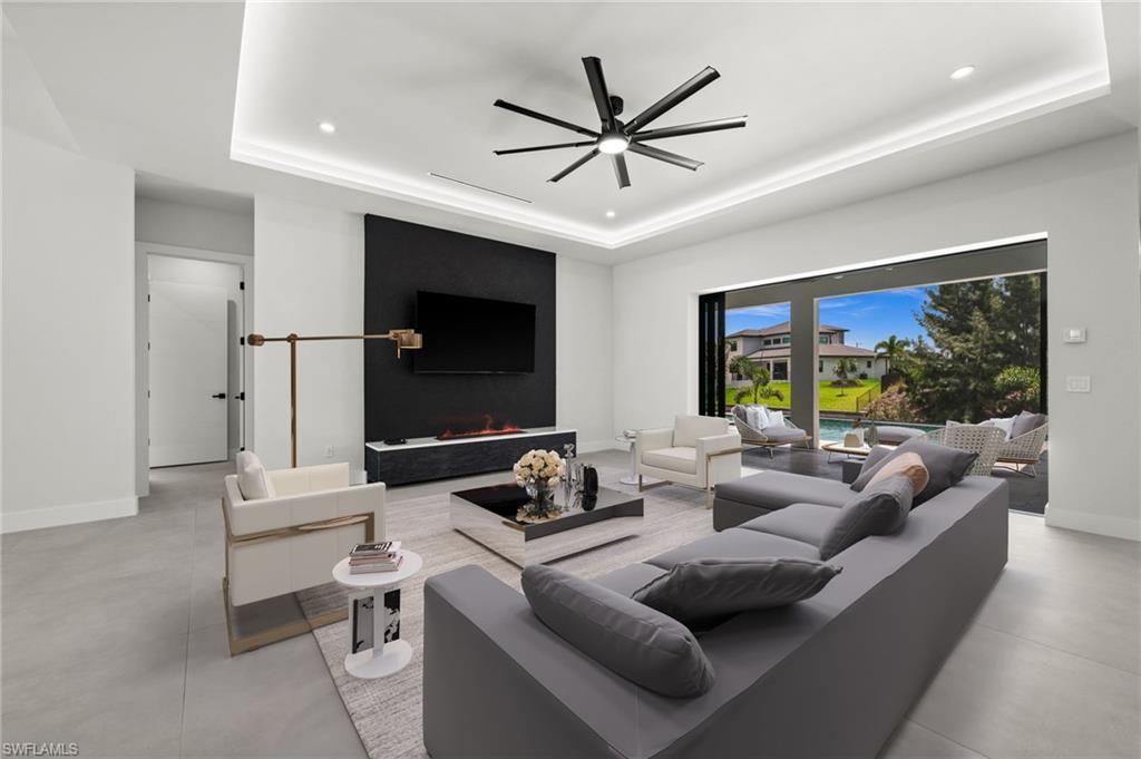 Living area featuring large format tile flooring, a recessed ceiling with cove lighting, and a contemporary ceiling fan