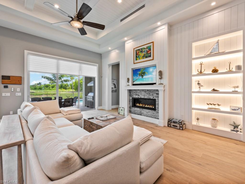 Living room featuring a raised ceiling, a stone fireplace, light wood-type flooring, and ceiling fan