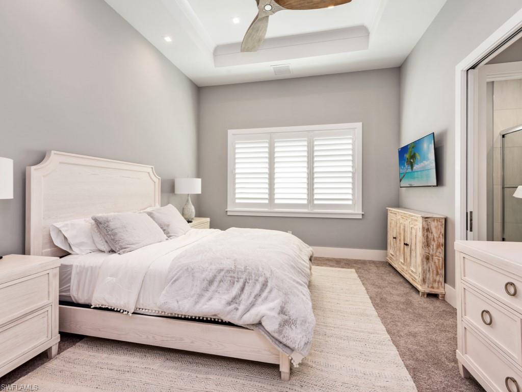 Carpeted bedroom featuring ceiling fan and a tray ceiling