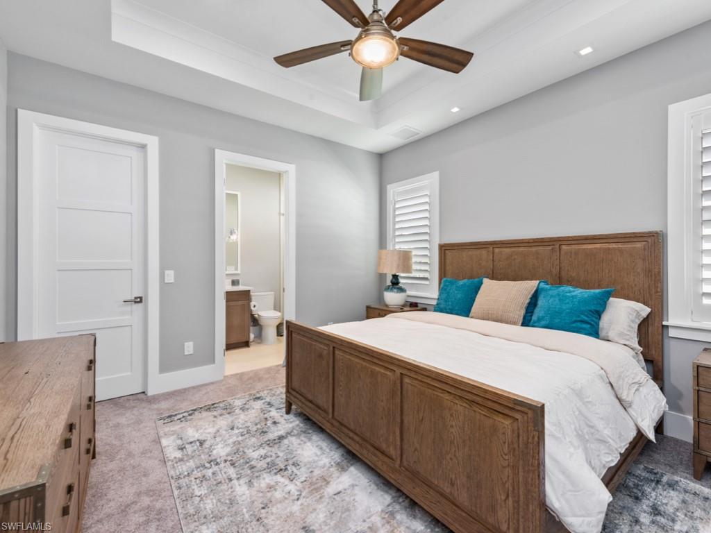 Bedroom featuring ceiling fan, light carpet, connected bathroom, and a tray ceiling
