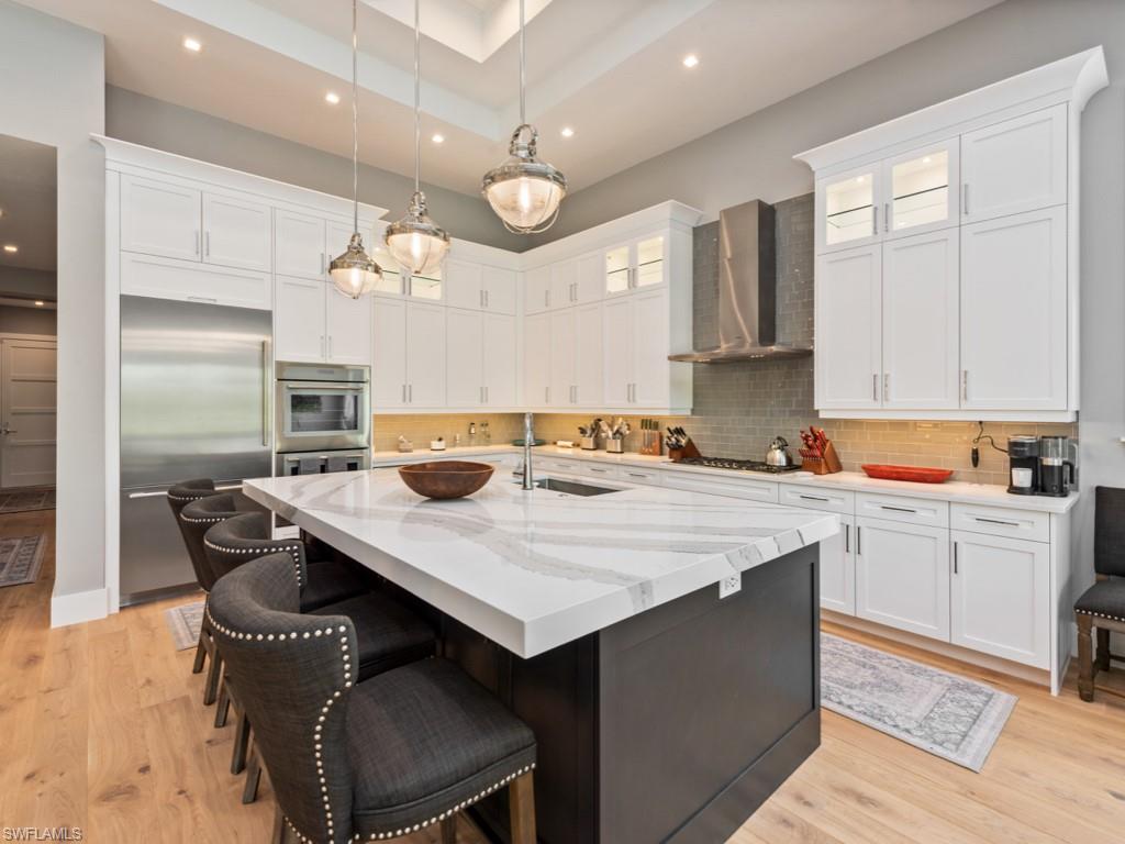 Kitchen with light wood-type flooring, stainless steel appliances, wall chimney exhaust hood, decorative backsplash, and sink