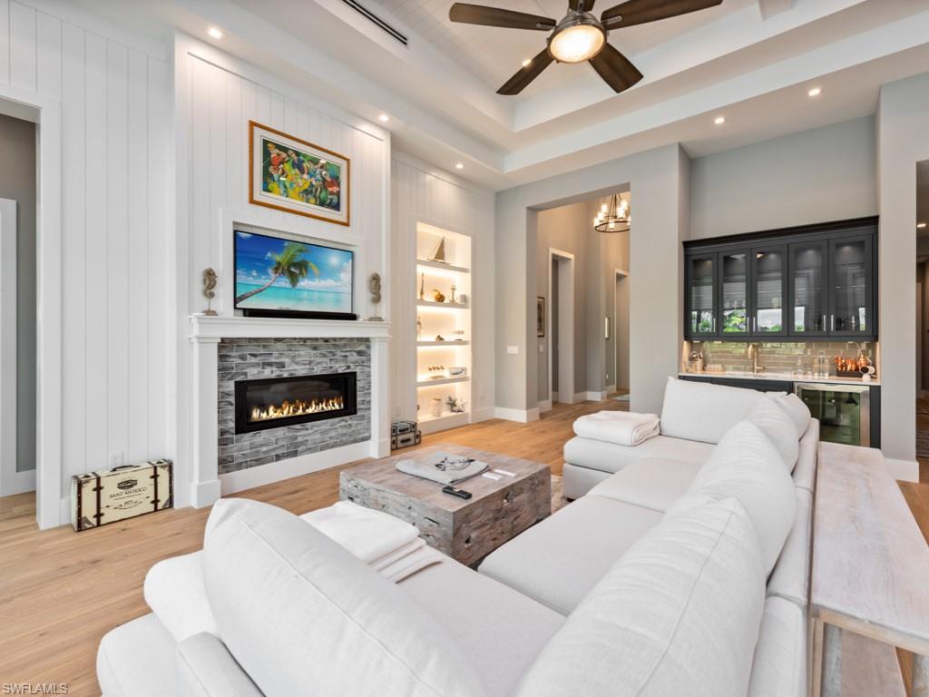 Living room with light hardwood / wood-style flooring, beverage cooler, ceiling fan with notable chandelier, built in shelves, and a fireplace