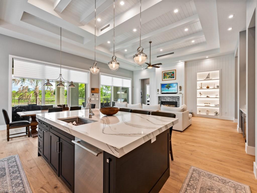 Kitchen featuring sink, a fireplace, pendant lighting, a kitchen island with sink, and light wood-type flooring