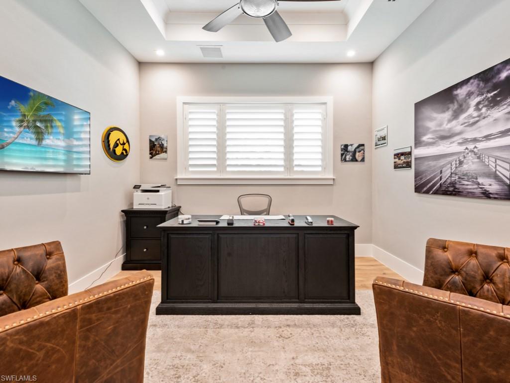 Home office with a tray ceiling, light hardwood / wood-style flooring, and ceiling fan