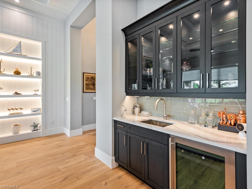 Bar featuring light hardwood / wood-style flooring, tasteful backsplash, beverage cooler, light stone countertops, and sink