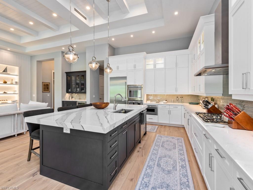 Kitchen with wall chimney range hood, an island with sink, sink, beam ceiling, and backsplash