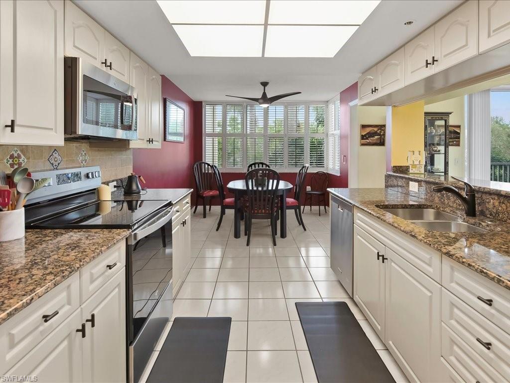Kitchen with stainless steel appliances, dark stone counters, light tile patterned floors, white cabinets, and ceiling fan