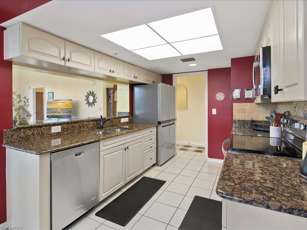 Kitchen with stainless steel appliances, dark stone counters, light tile patterned floors, and backsplash