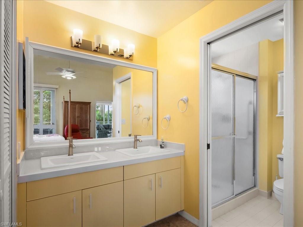 Ensuite bathroom with a shower stall, double vanity, ceiling fan, and light tile patterned floors
