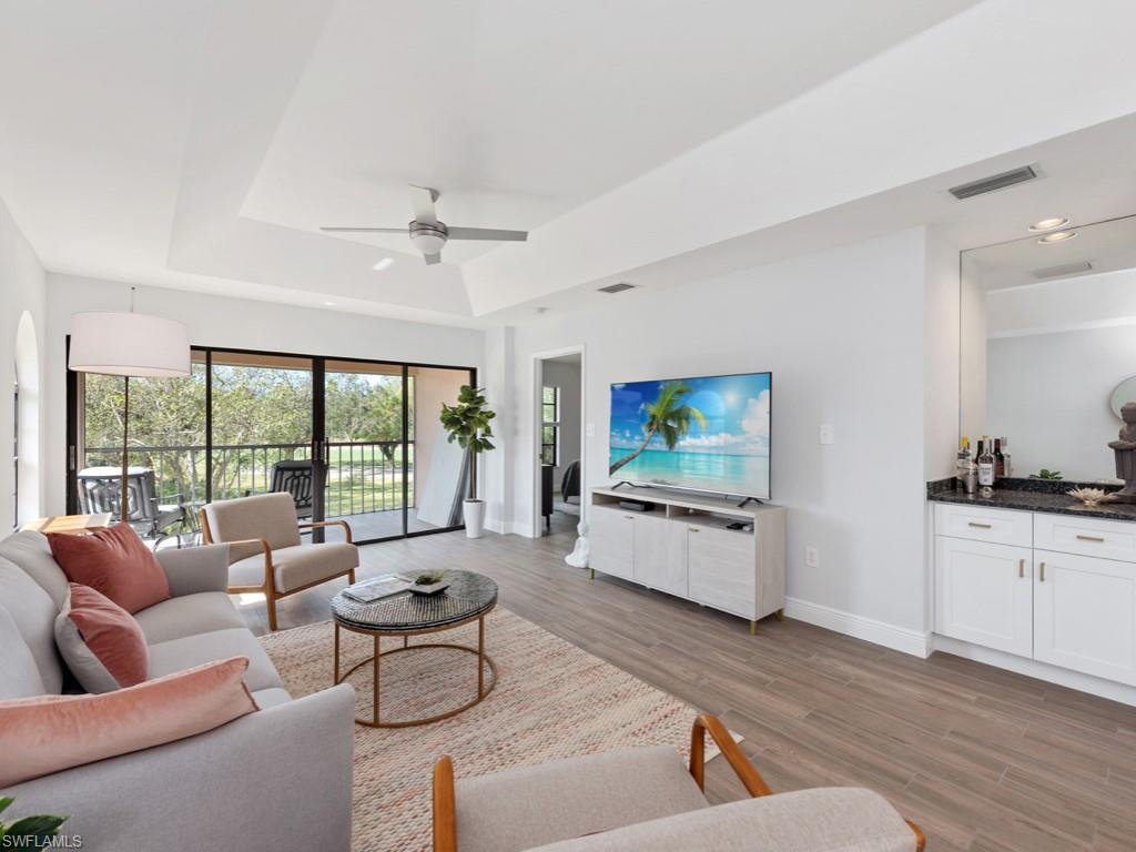 Living room with ceiling fan, a raised ceiling, and light wood-type flooring
